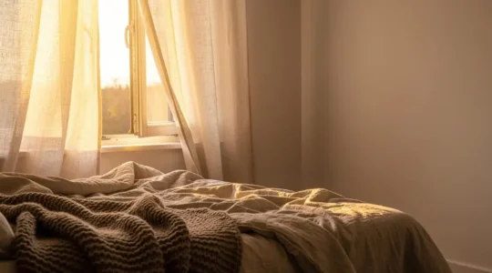Dormitorio luminoso con cortinas de lino, ropa de cama de algodón orgánico y una manta de lana gruesa creando una atmósfera cálida y natural